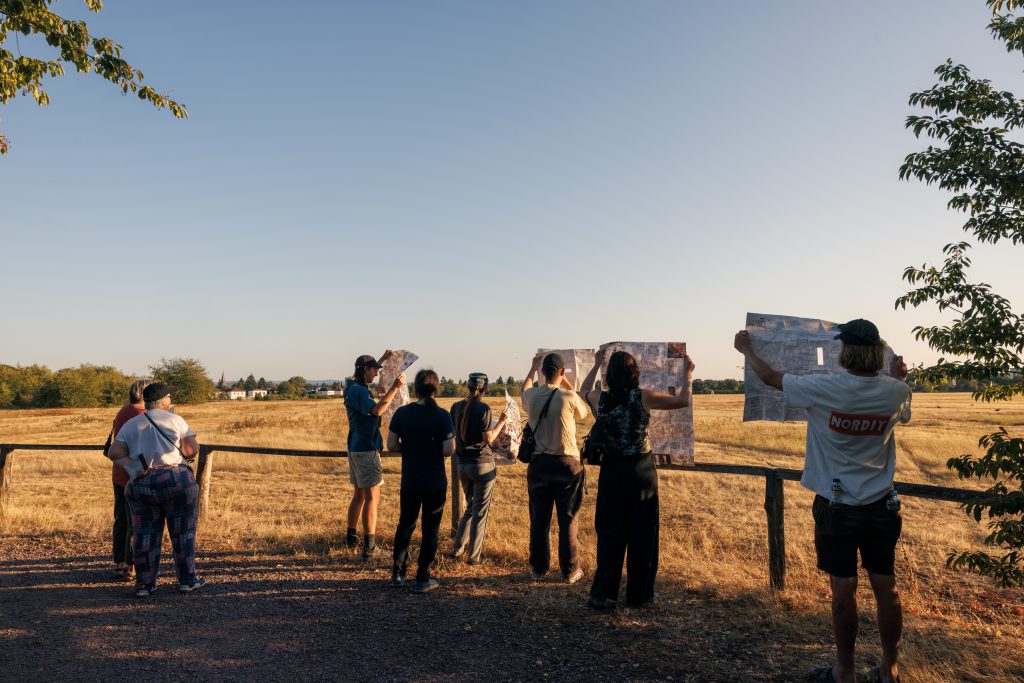 Teilnehmende der Performance in Form eines Spaziergangs über den Alten Flugplatz Karlsruhe - Copyright: 2 Flächen bewegen, 50 km/h, Schritttempo, Josefine Pilar Scheu, Nis Petersen, Isabel Motz, 2026. © Stadt Karlsruhe, Kulturamt, Foto: Felix Grünschloß