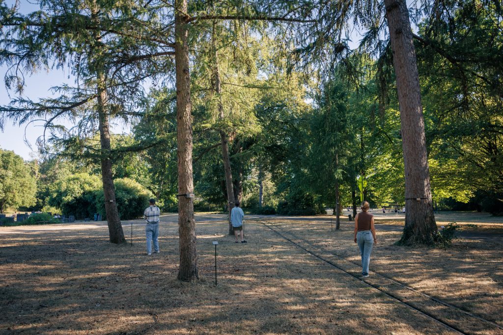 Ausschnitt von fünf Bäumen der Soundinstallation „555Hz“ mit 3 Besucher:innen - Copyright: 555 Hz, Antoine Bertin, 2026. © Stadt Karlsruhe, Kulturamt, Foto: Felix Grünschloß