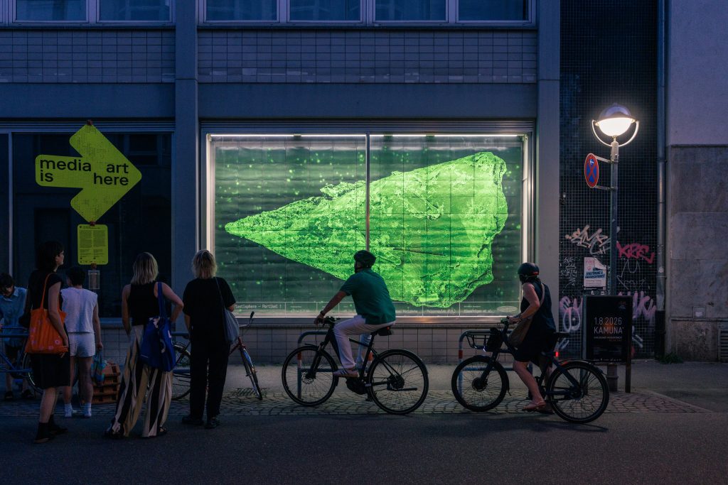Rasterelektronenmikroskop-Aufnahme eines Mikroplastikpartikels im Schaufenster des Museum am Markt mit Besuchenden auf Fahrrädern. - Copyright: Live from Plastisphere, Vera Gärtner, 2026. © Stadt Karlsruhe, Kulturamt, Foto: Felix Grünschloß