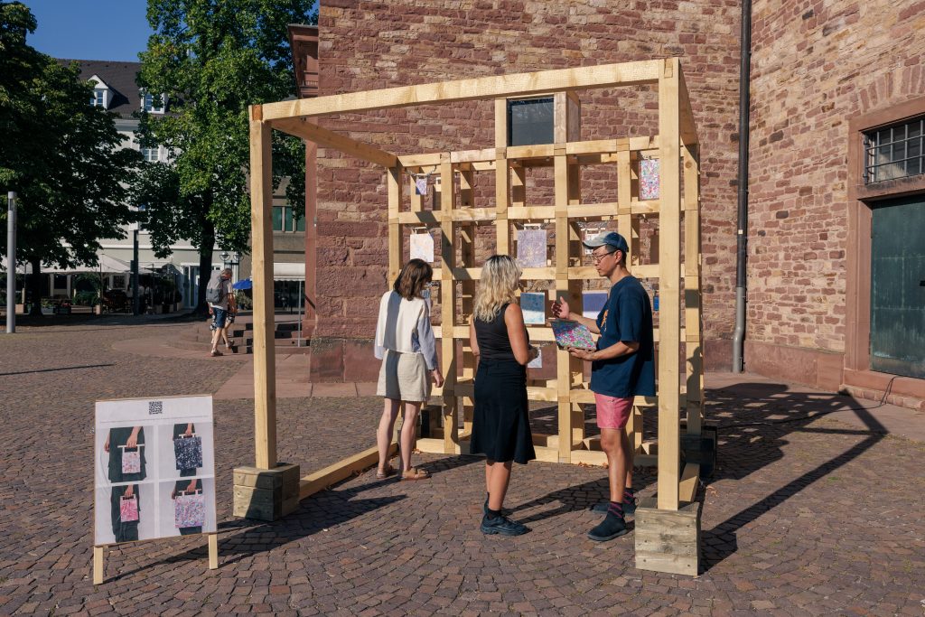 Der Künstler SangDoo Nam (rechts) erklärt in seiner Arbeit „Urban Flowers“ den Tausch von Kunstwerk gegen Geschichte. - Copyright: Urban Flowers, SangDoo Nam, 2026. © Stadt Karlsruhe, Kulturamt, Foto: Felix Grünschloß
